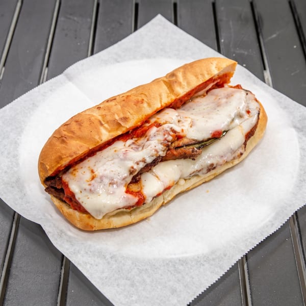 A long Italian sub sandwich with melted cheese and red sauce on white parchment paper.