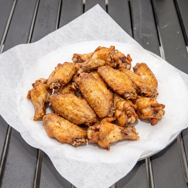 A platter of golden-brown chicken wings, glistening with sauce, served on white parchment paper.