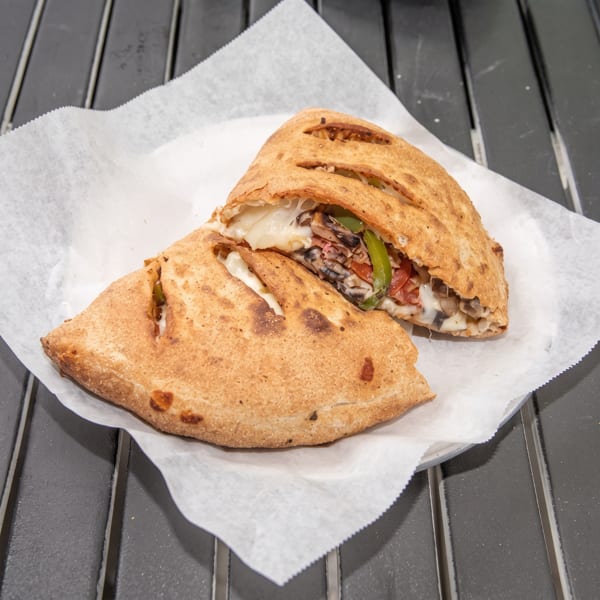 Two halves of a calzone filled with melted cheese, mushrooms, and green peppers on parchment paper.