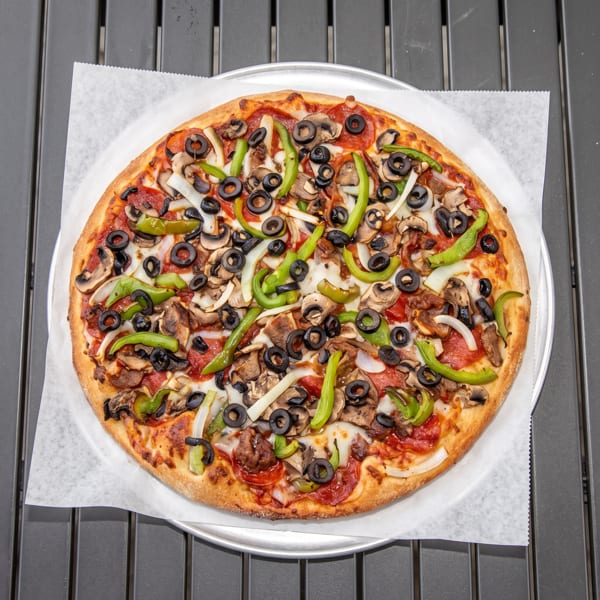 A whole pizza with pepperoni, mushrooms, black olives, green peppers, and onions on a metal tray.