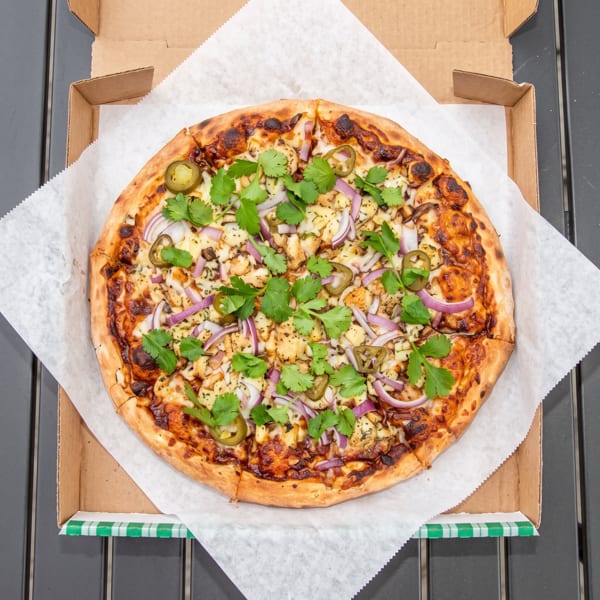 Overhead view of a BBQ chicken pizza with red onions, jalapeños, and cilantro in a box.