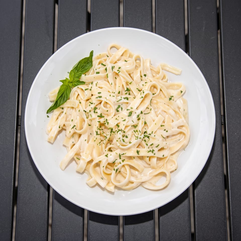 Creamy fettuccine Alfredo topped with chopped herbs and fresh basil on a white plate.