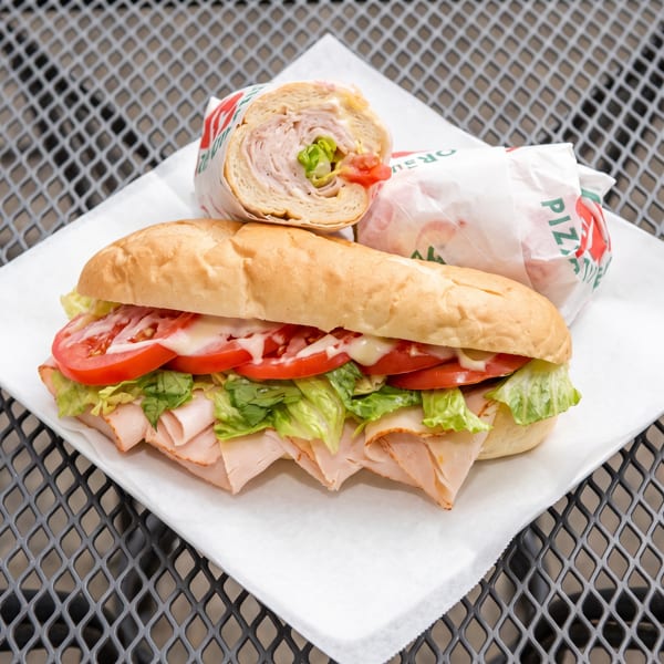 A turkey sub sandwich with lettuce, tomatoes, and mayonnaise, with a wrapped half sub behind it.
